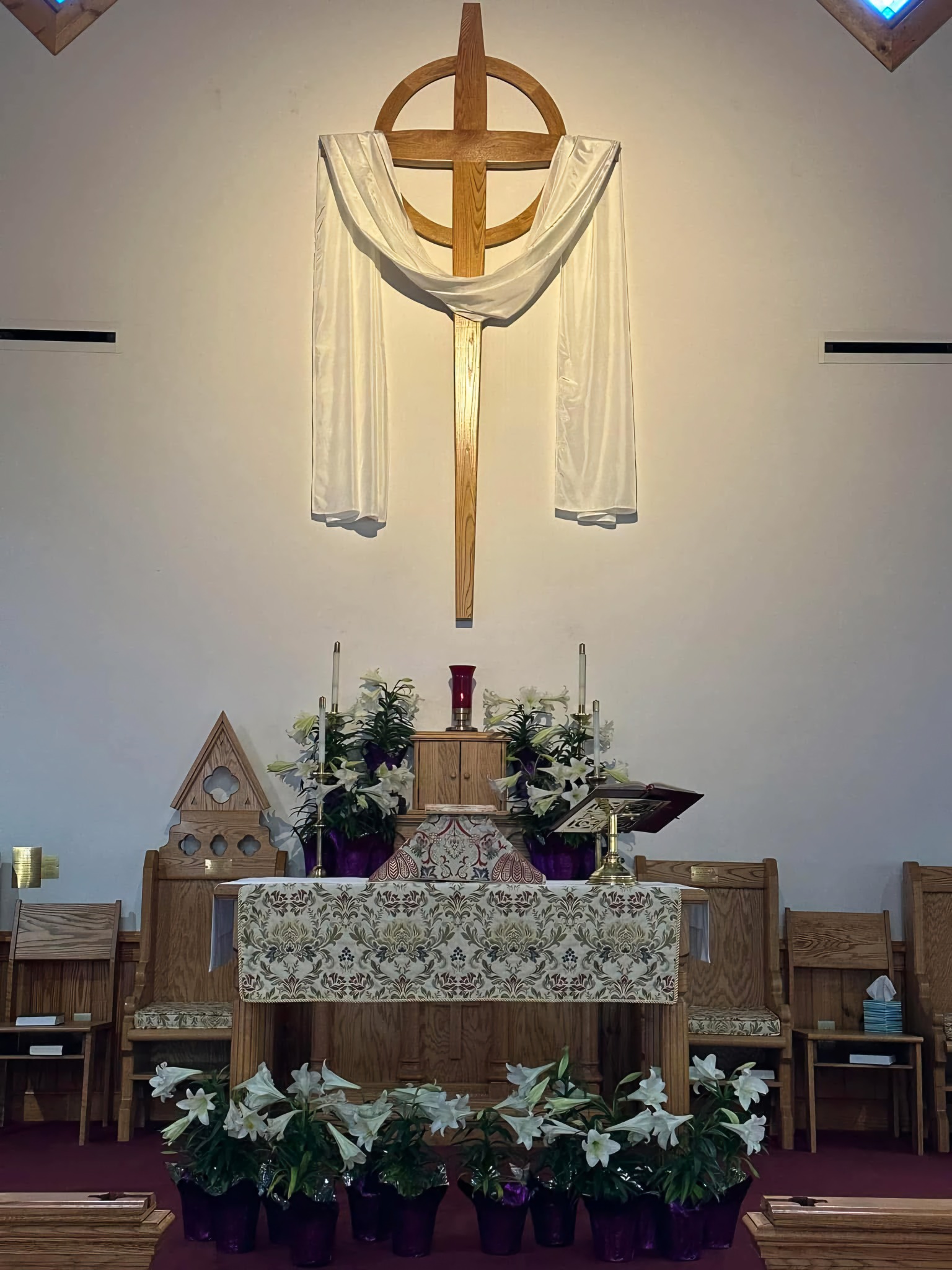 Wooden cross draped in white above the Christ Church altar, surrounded by lilies